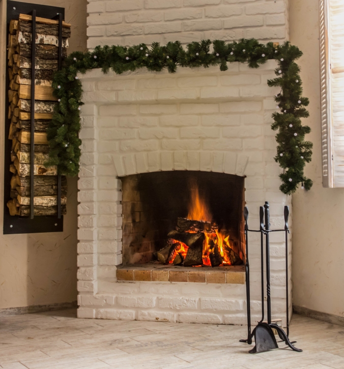 Cheminée en briques blanches avec feu allumé et rangement de bûches, idéale pour chauffage au bois et entretien régulier